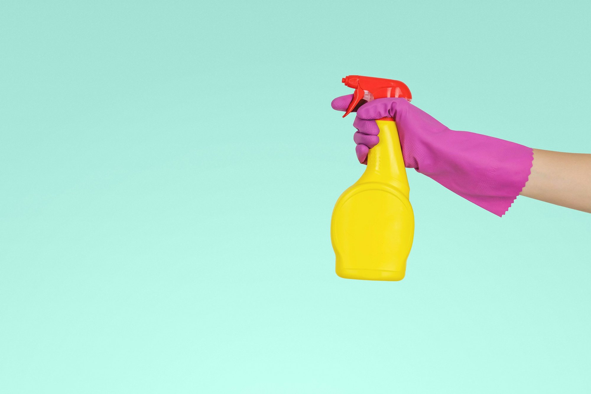 Gloved hand holding a yellow spray bottle against an aqua background