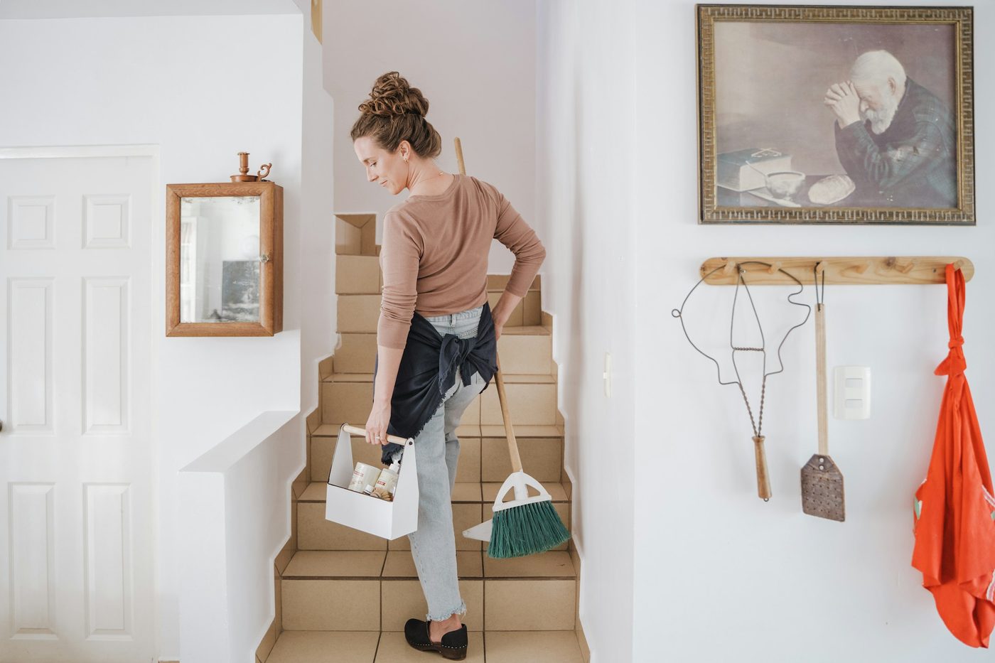 Woman carrying a cleaning caddy and broom up stairs